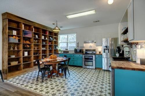 kitchen featuring wooden counters, appliances with stainless steel finishes, sink, blue cabinetry, and white cabinets