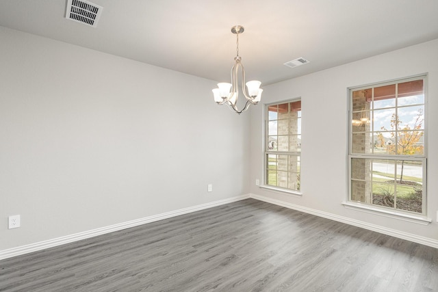 unfurnished room with a healthy amount of sunlight, dark hardwood / wood-style flooring, and a chandelier