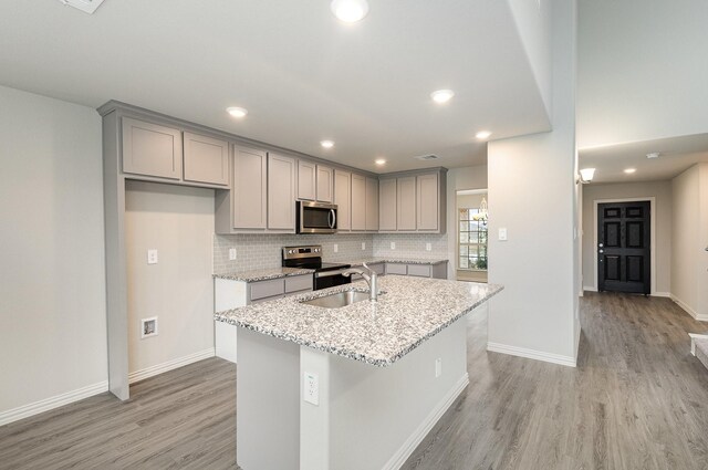 kitchen with sink, stainless steel appliances, light stone counters, light hardwood / wood-style floors, and a kitchen island with sink