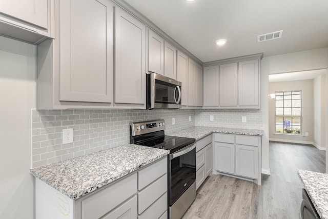 kitchen featuring gray cabinetry, light stone counters, backsplash, light hardwood / wood-style floors, and appliances with stainless steel finishes