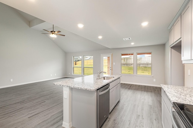 kitchen featuring hardwood / wood-style floors, a center island with sink, sink, appliances with stainless steel finishes, and light stone counters