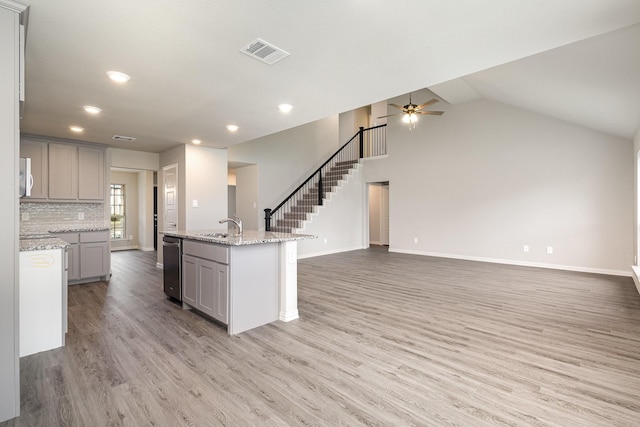 kitchen featuring light hardwood / wood-style flooring, gray cabinetry, a kitchen island with sink, light stone countertops, and stainless steel dishwasher