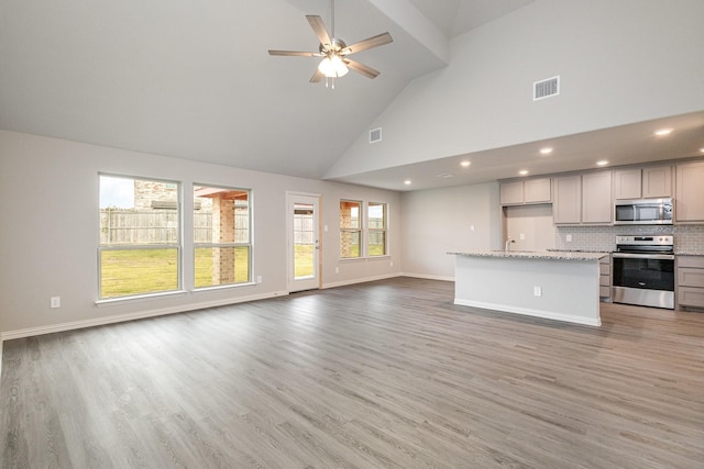 kitchen featuring light stone countertops, appliances with stainless steel finishes, backsplash, a kitchen island with sink, and gray cabinets