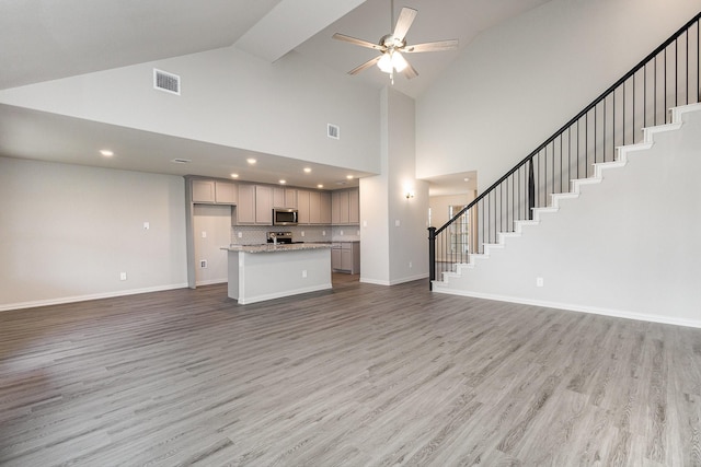 unfurnished living room with hardwood / wood-style floors, high vaulted ceiling, and ceiling fan