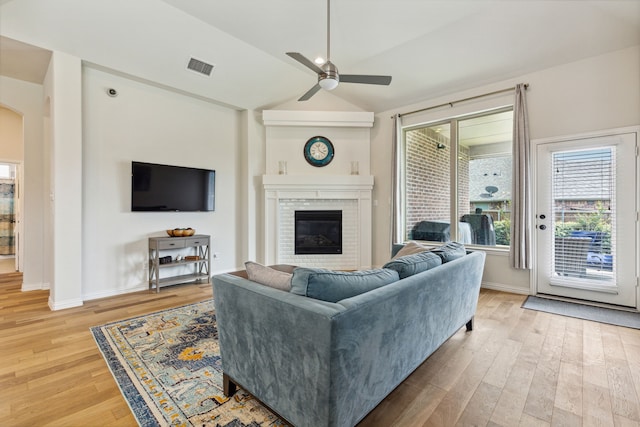 living room with ceiling fan, vaulted ceiling, wood-type flooring, and a brick fireplace