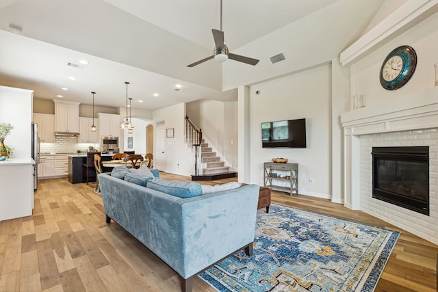 living room featuring a fireplace, light hardwood / wood-style floors, vaulted ceiling, and ceiling fan