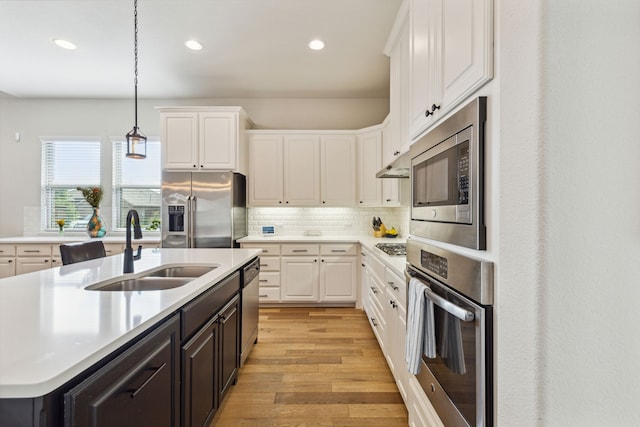 kitchen featuring appliances with stainless steel finishes, a kitchen island with sink, sink, decorative light fixtures, and white cabinetry