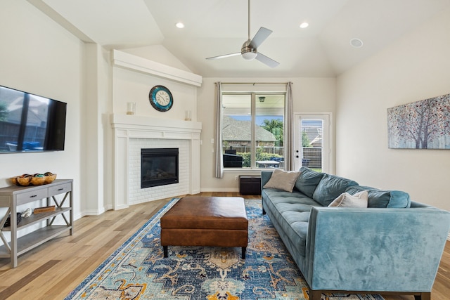 living room featuring ceiling fan, a fireplace, light hardwood / wood-style floors, and vaulted ceiling