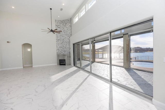 unfurnished living room featuring arched walkways, marble finish floor, a fireplace, and baseboards