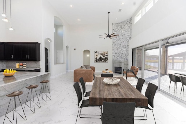 dining room with arched walkways, marble finish floor, recessed lighting, a large fireplace, and baseboards