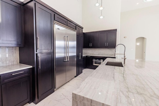 kitchen featuring arched walkways, stainless steel appliances, a sink, marble finish floor, and light stone countertops