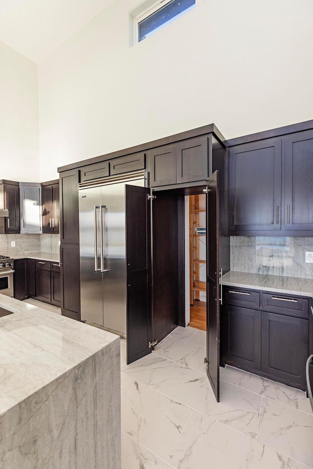 kitchen with marble finish floor, backsplash, a towering ceiling, and high quality appliances