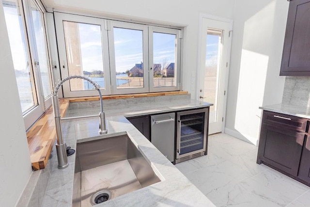 kitchen featuring beverage cooler, a sink, marble finish floor, and light stone countertops