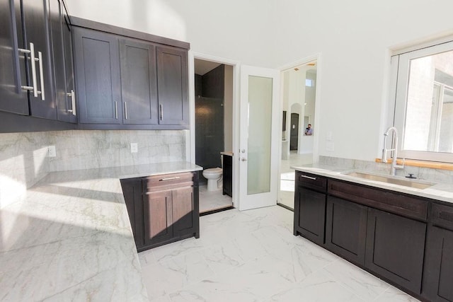 kitchen featuring arched walkways, a sink, marble finish floor, dark brown cabinets, and decorative backsplash