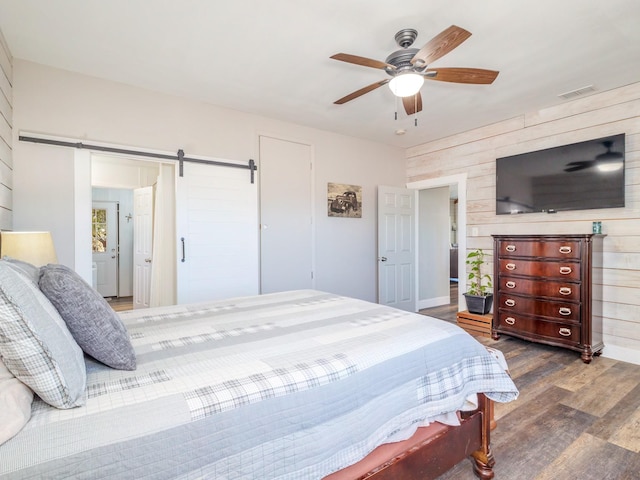 bedroom with a barn door, dark wood-type flooring, and ceiling fan