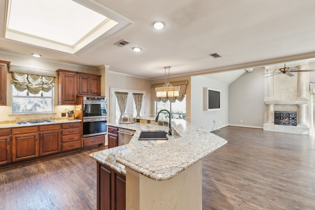 kitchen with pendant lighting, a center island with sink, sink, a tiled fireplace, and appliances with stainless steel finishes