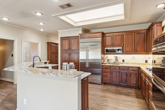 kitchen featuring light stone countertops, sink, a kitchen island with sink, and built in appliances