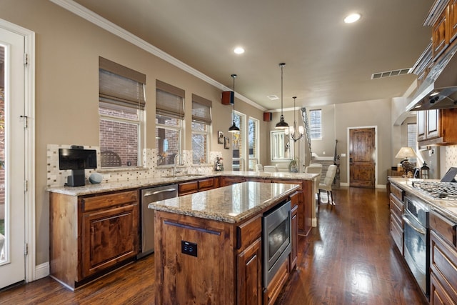 kitchen featuring a center island, sink, dark wood-type flooring, stainless steel appliances, and decorative light fixtures