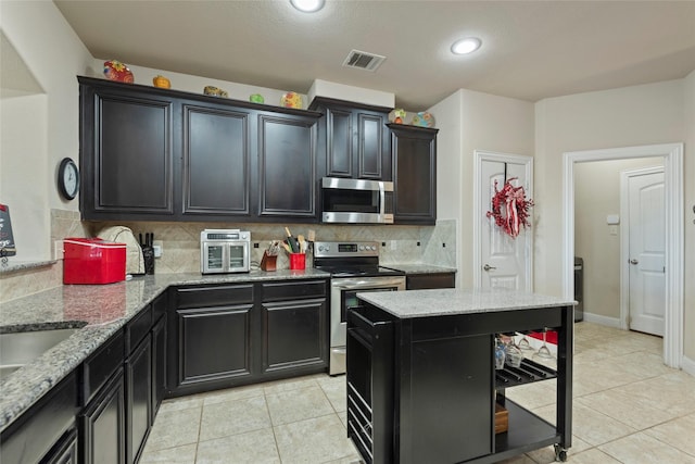 kitchen with tasteful backsplash, appliances with stainless steel finishes, light stone countertops, and light tile patterned floors