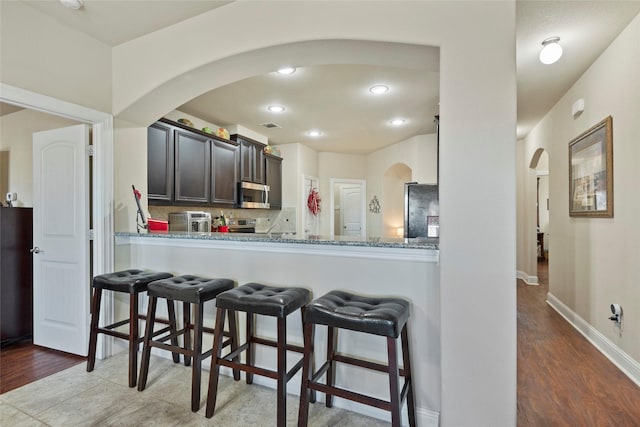 kitchen featuring hardwood / wood-style flooring, backsplash, stainless steel appliances, light stone counters, and kitchen peninsula