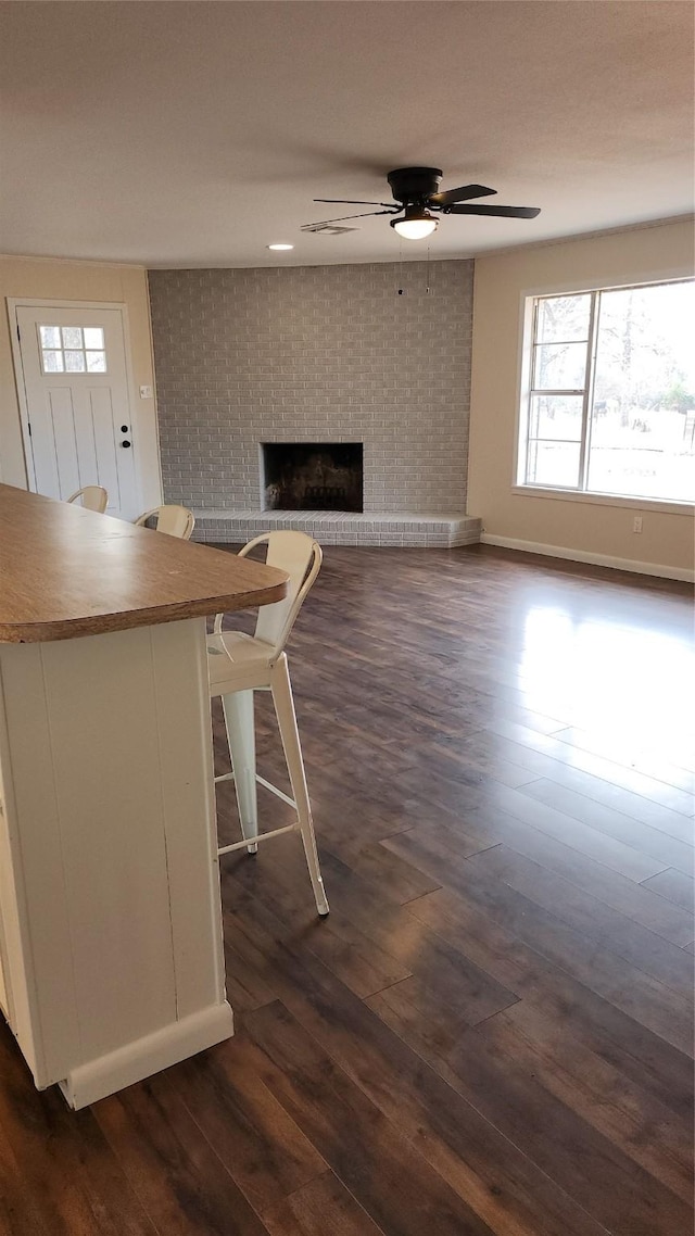 unfurnished living room featuring a brick fireplace, dark wood-type flooring, and ceiling fan