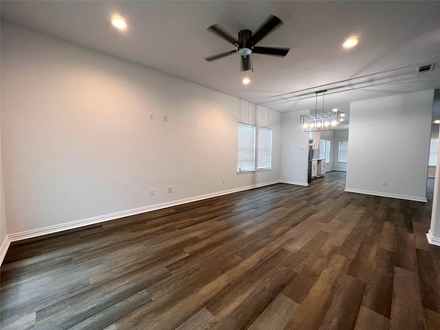 empty room featuring ceiling fan with notable chandelier and dark hardwood / wood-style floors