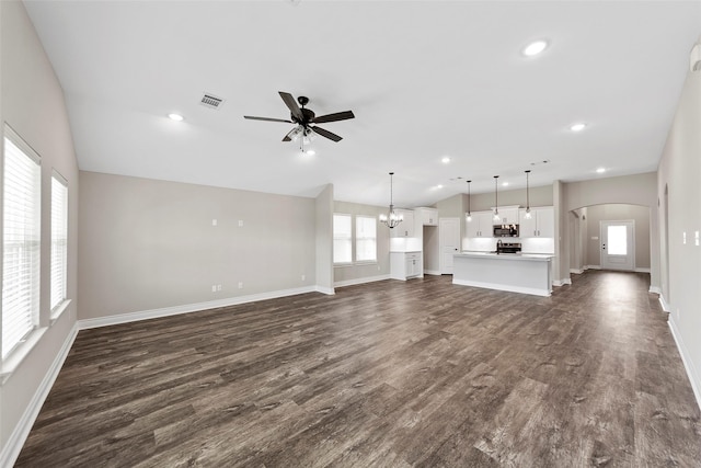 unfurnished living room with ceiling fan with notable chandelier, lofted ceiling, dark wood-type flooring, and a wealth of natural light