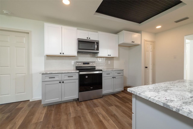 kitchen with appliances with stainless steel finishes, white cabinets, dark hardwood / wood-style flooring, and a tray ceiling