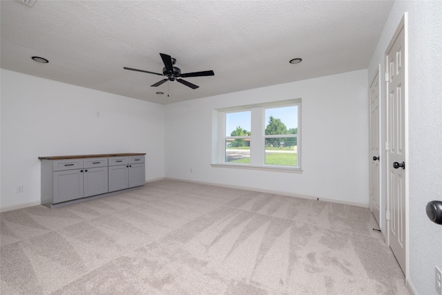 unfurnished bedroom with ceiling fan, light colored carpet, and a textured ceiling