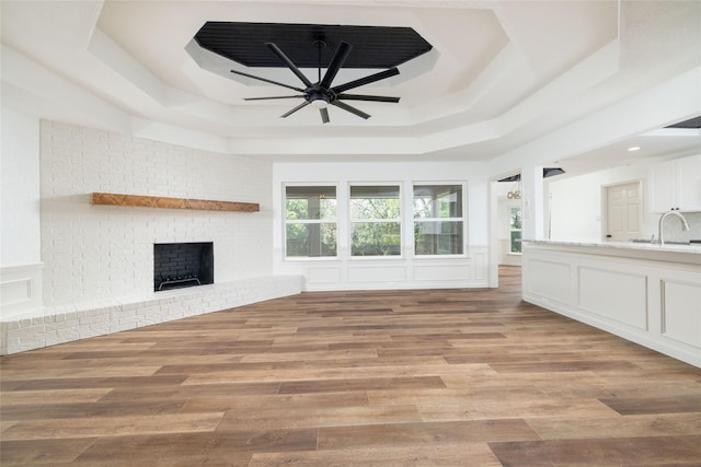 unfurnished living room with a fireplace, a tray ceiling, and light wood-type flooring