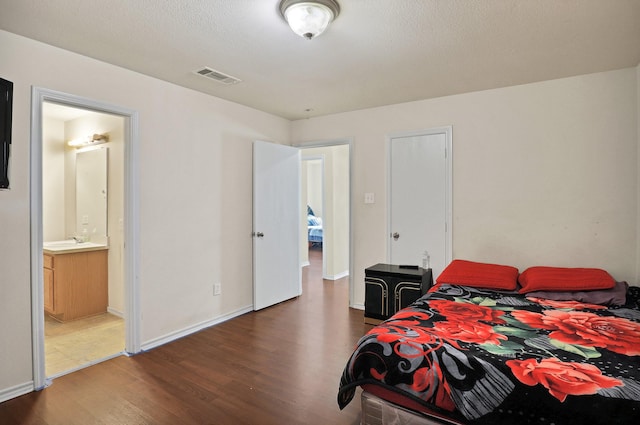 bedroom featuring dark hardwood / wood-style floors, ensuite bath, and sink