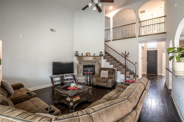 living room with ceiling fan, dark hardwood / wood-style flooring, a high ceiling, and a brick fireplace