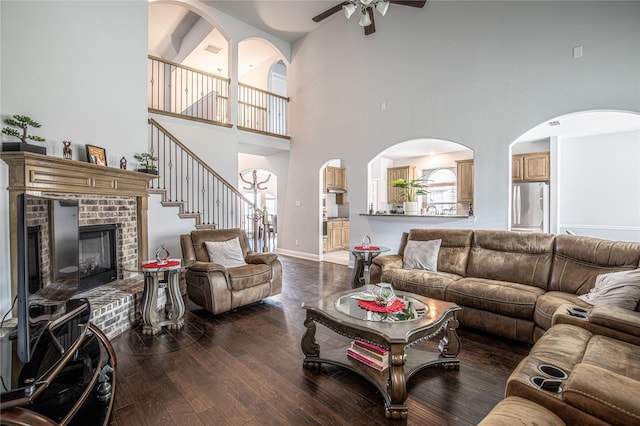 living room featuring a fireplace, a high ceiling, ceiling fan, and wood-type flooring