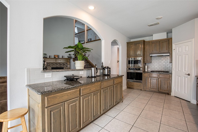 kitchen with decorative backsplash, light tile patterned floors, stainless steel appliances, and dark stone counters