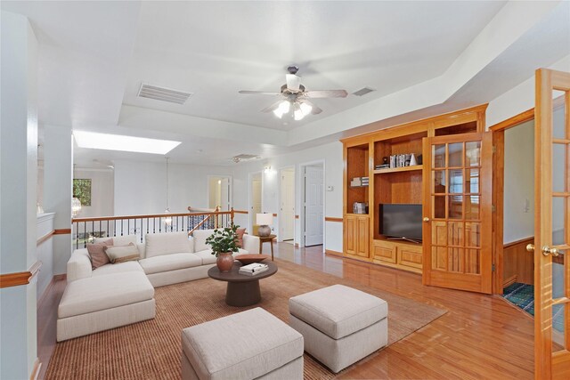 living room with hardwood / wood-style floors, a tray ceiling, built in features, and ceiling fan