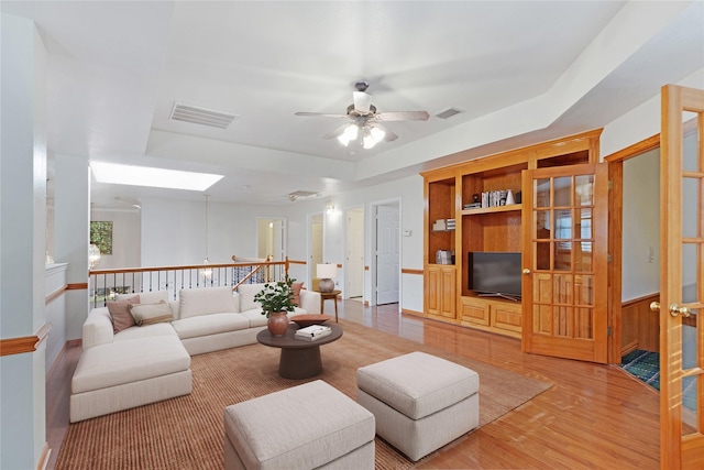 living area featuring built in shelves, a tray ceiling, a skylight, visible vents, and wood finished floors