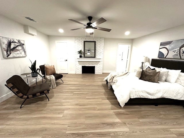 bedroom with ceiling fan, light hardwood / wood-style floors, and a brick fireplace