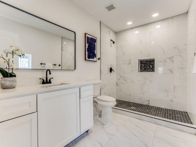 bathroom featuring a tile shower, vanity, and toilet