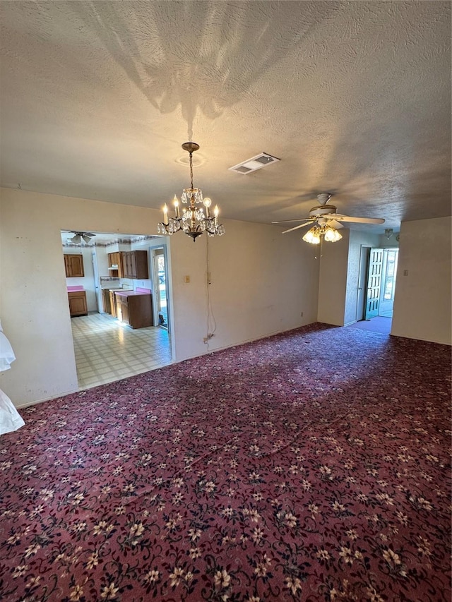 empty room with light carpet, a textured ceiling, and ceiling fan with notable chandelier