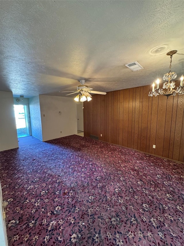 unfurnished room featuring ceiling fan with notable chandelier, a textured ceiling, carpet floors, and wood walls