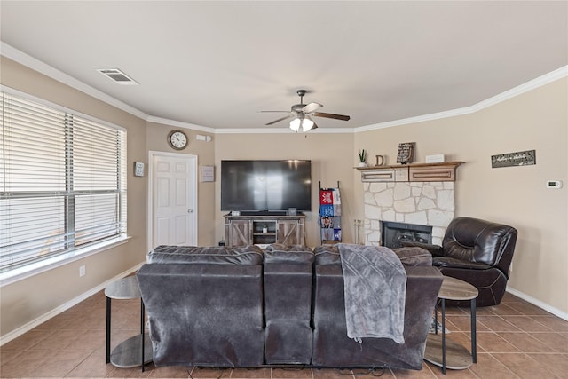 living room with tile patterned flooring, a stone fireplace, ceiling fan, and crown molding