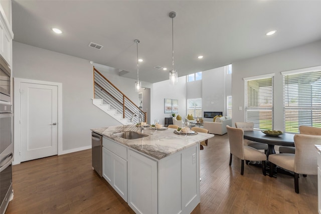 kitchen with light stone countertops, stainless steel dishwasher, sink, white cabinets, and an island with sink