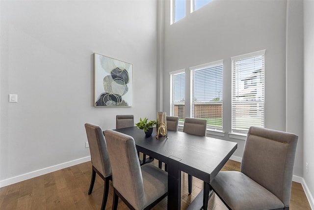 dining space featuring a towering ceiling and dark wood-type flooring