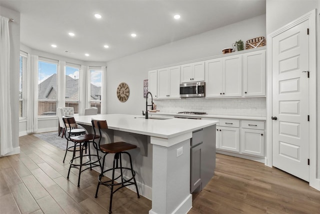 kitchen featuring tasteful backsplash, a kitchen island with sink, sink, hardwood / wood-style floors, and white cabinetry