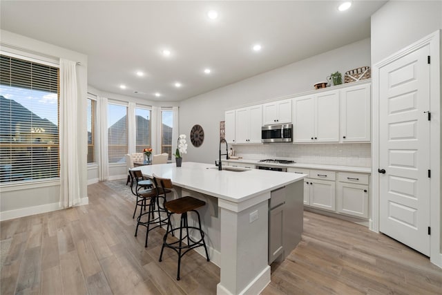 kitchen with a center island with sink, white cabinets, sink, light wood-type flooring, and appliances with stainless steel finishes