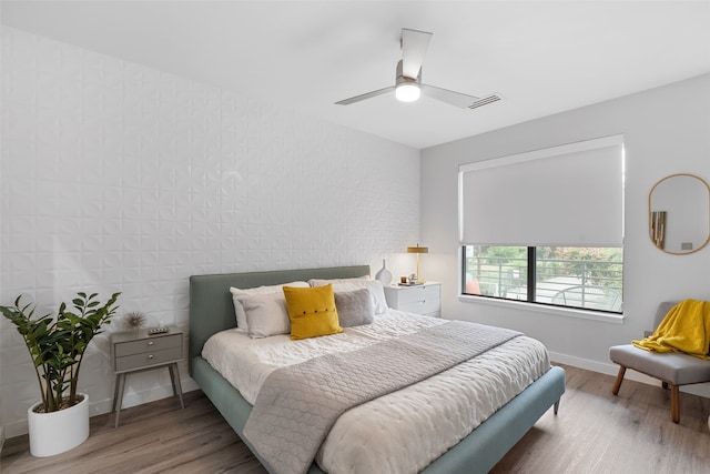 bedroom with ceiling fan, wood-type flooring, and brick wall