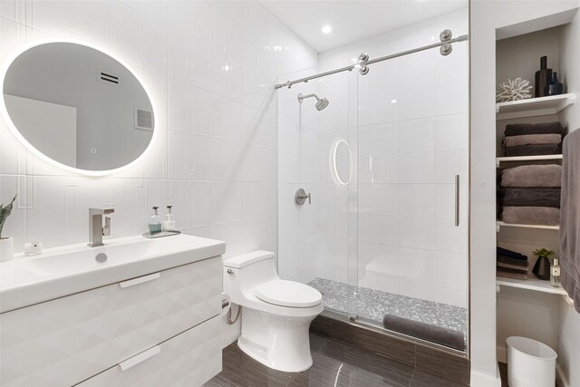 bathroom featuring vanity, toilet, a shower with door, and tile walls