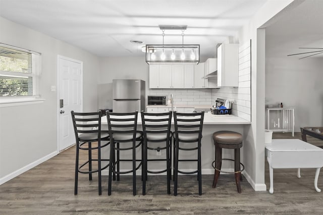 kitchen with kitchen peninsula, tasteful backsplash, a breakfast bar area, white cabinetry, and stainless steel refrigerator