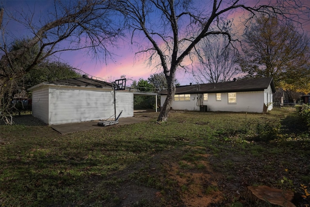 back house at dusk with a lawn and central AC