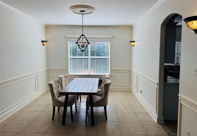 dining area with wainscoting, arched walkways, a decorative wall, and light tile patterned floors